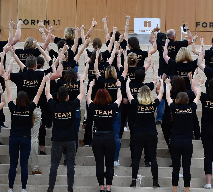 Gruppenfoto des Teams von hinten. Personen stehen auf Stufen und strecken die Fäuste gen Himmel.